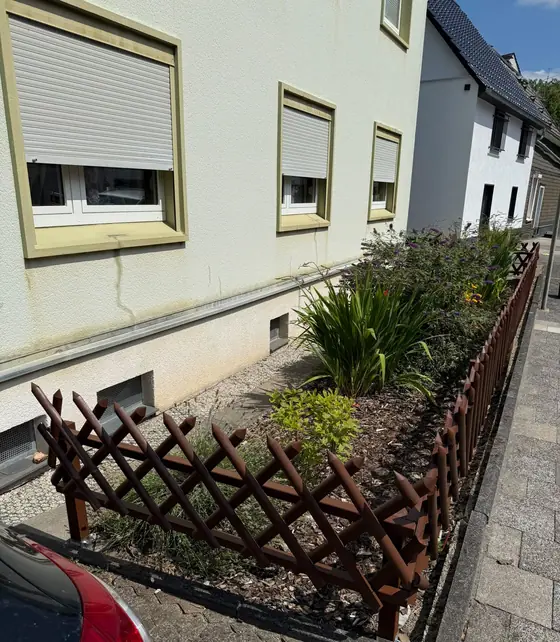 Neu bepflanztes Beet mit Rankgitter vor der Fassade eines Wohnhauses
