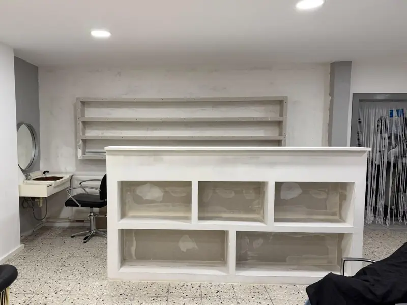 Unverkleideter Empfangstresen im Rohbau vor einer unfertigen Wand mit leeren Regalböden