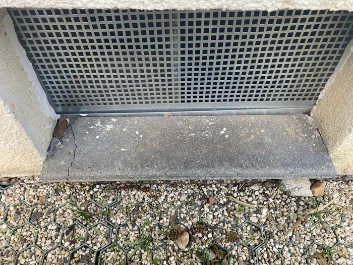 Rissiger, beschädigter Betonsockel unter einem Kellerfenstergitter